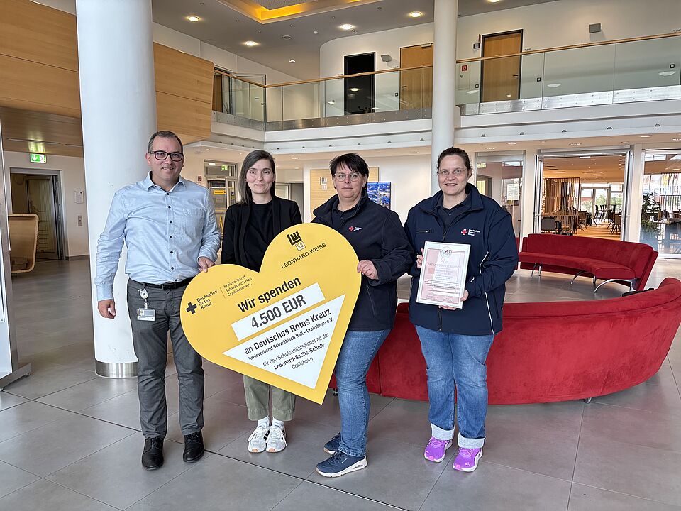4 Menschen lächeln in die Kamera, ein symbolischer Spendenscheck in Herzform wird überreicht.