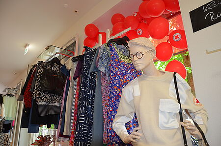 Schaufensterpuppe mit DRK-Pulli vor mit Luftballons geschmücktem Fenster